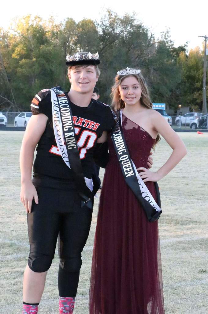 Chaston Mouser and Justice Lee-Jones with crowns and sashes for Homecoming King and Queen on the football field with trees behind them